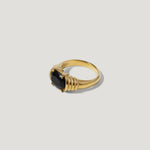 Gold ring with a large black gemstone and textured band on a light background