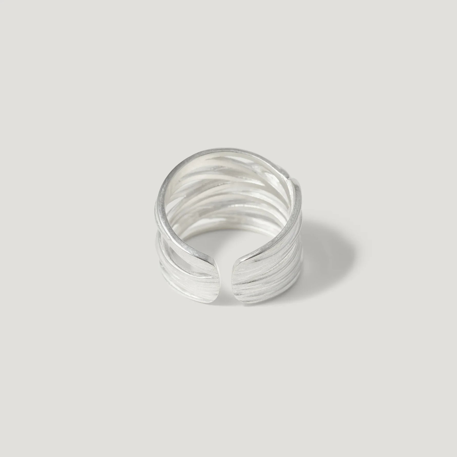 Textured open band silver ring on plain light background, modern minimalist jewelry