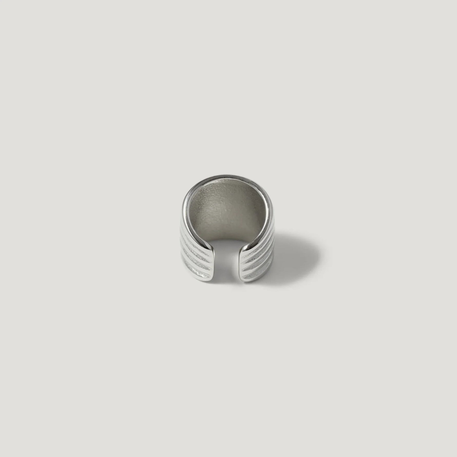 Textured silver ear cuff with grooved lines on a white background