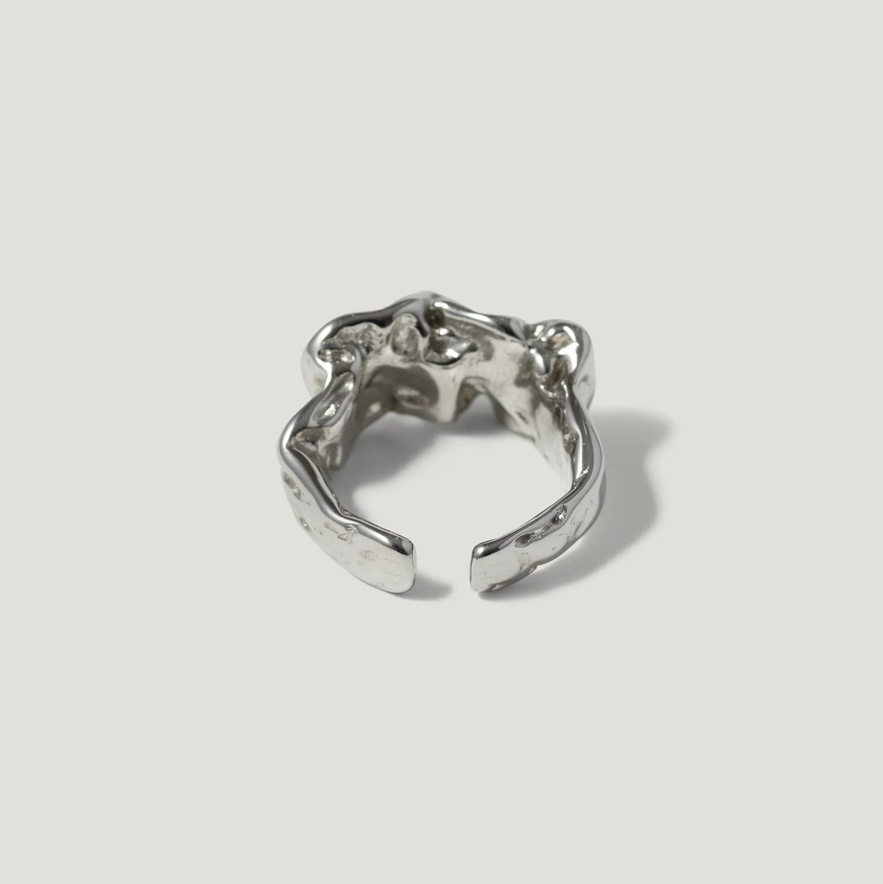 Textured silver open ring with organic, sculptural design on a plain background