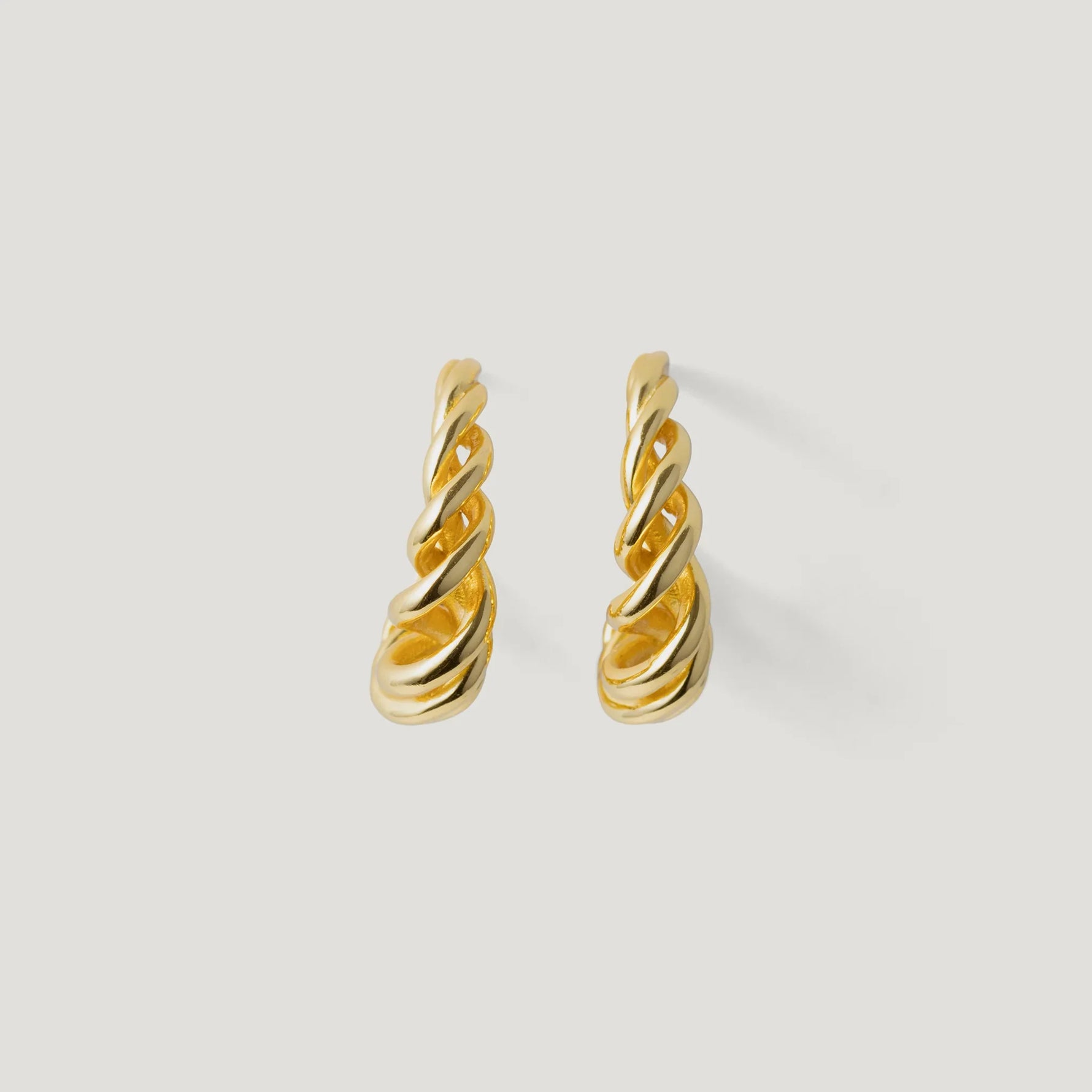 Pair of gold twisted hoop earrings on white background, modern jewellery design