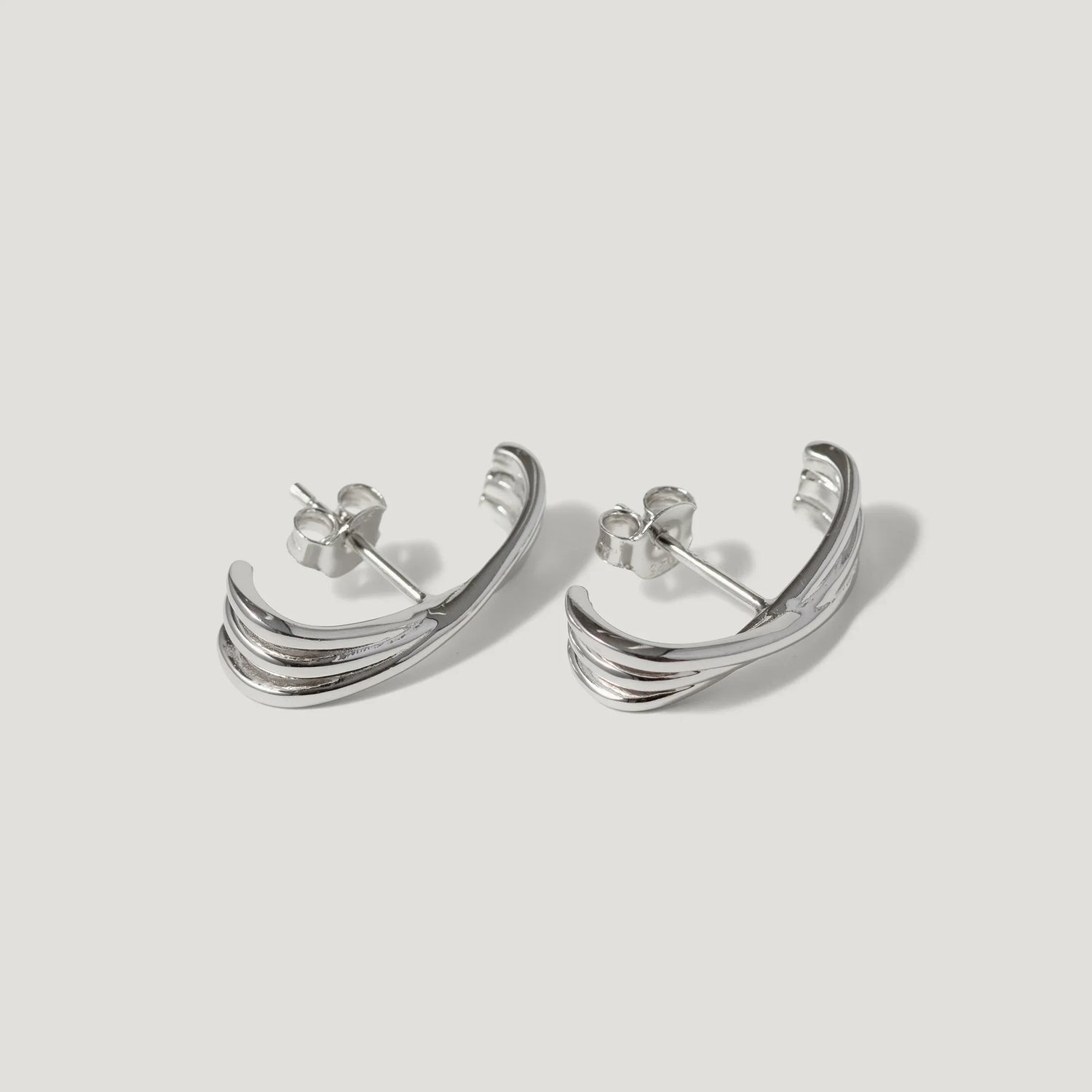 Pair of silver crescent-shaped stud earrings with layered curved design on white background