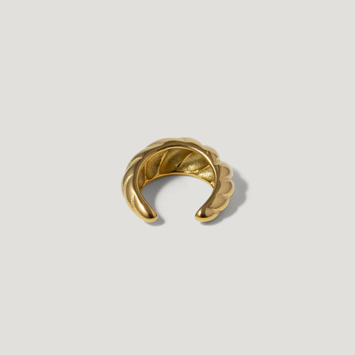 Gold textured ear cuff with twisted design on white background
