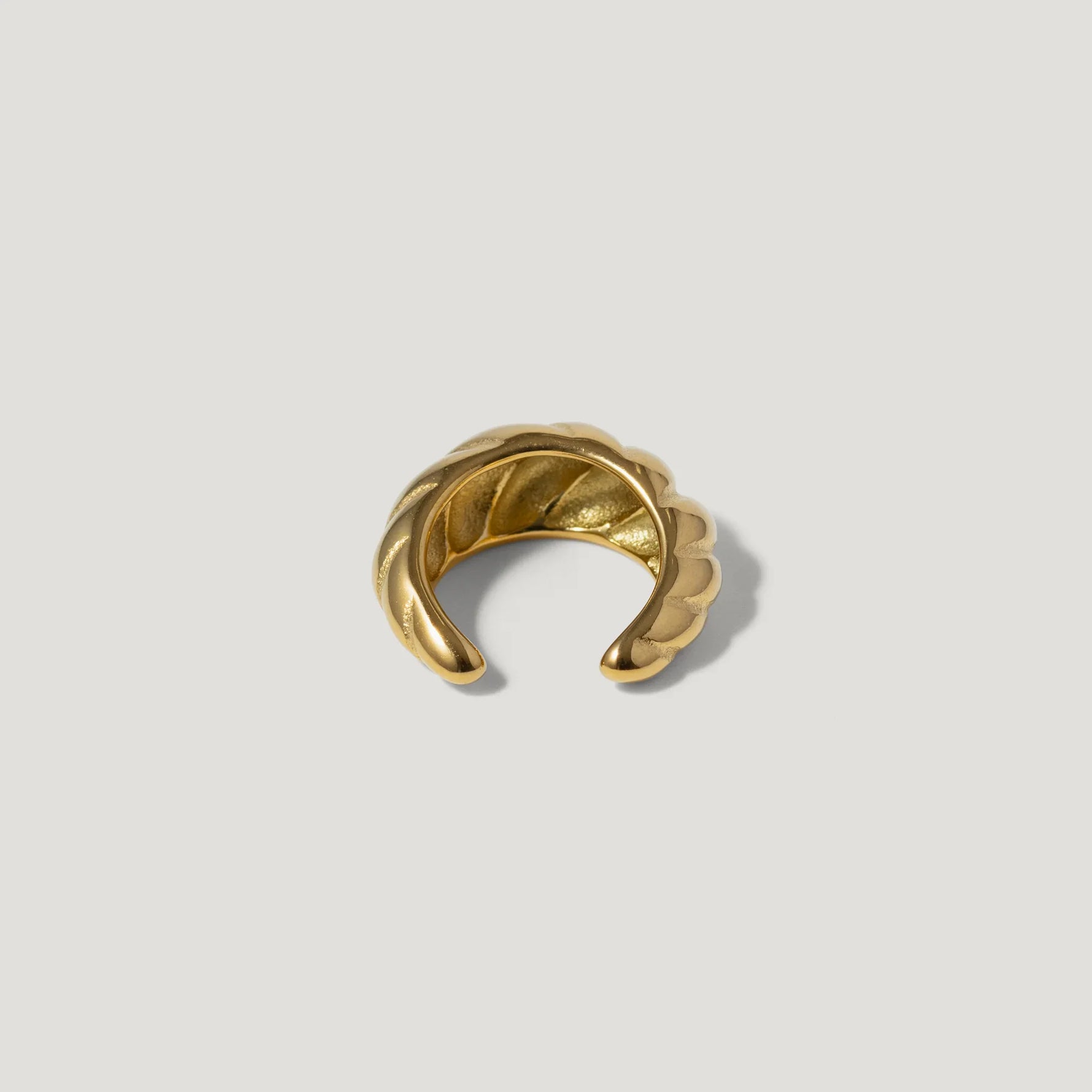 Gold textured ear cuff with twisted design on white background