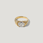 Gold ring with large round clear gemstone and textured setting on light background