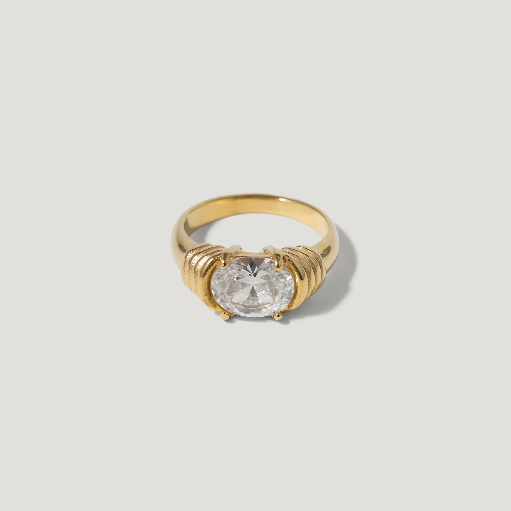 Gold ring with large round clear gemstone and textured setting on light background