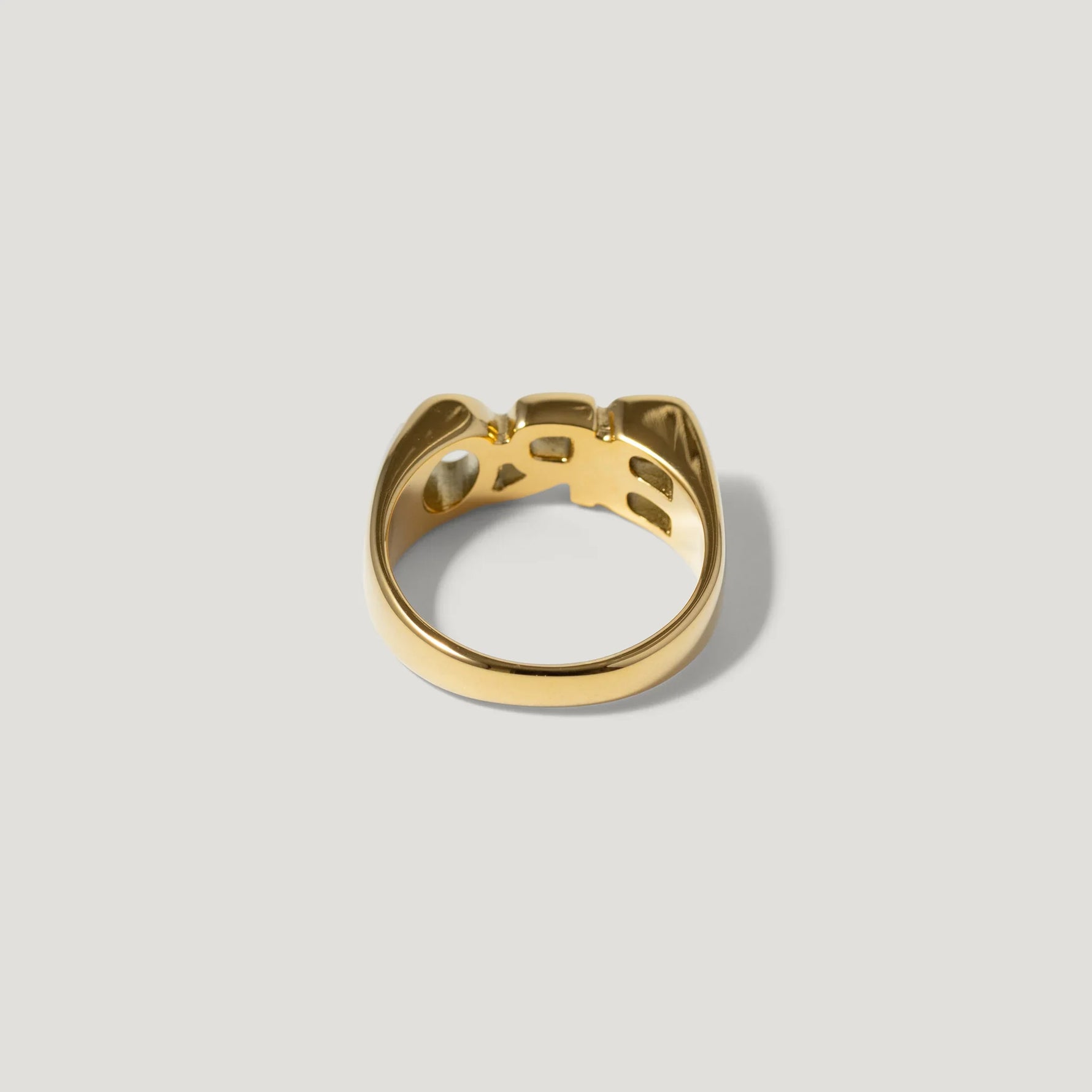 Polished gold statement ring with geometric cut-out design on a plain background