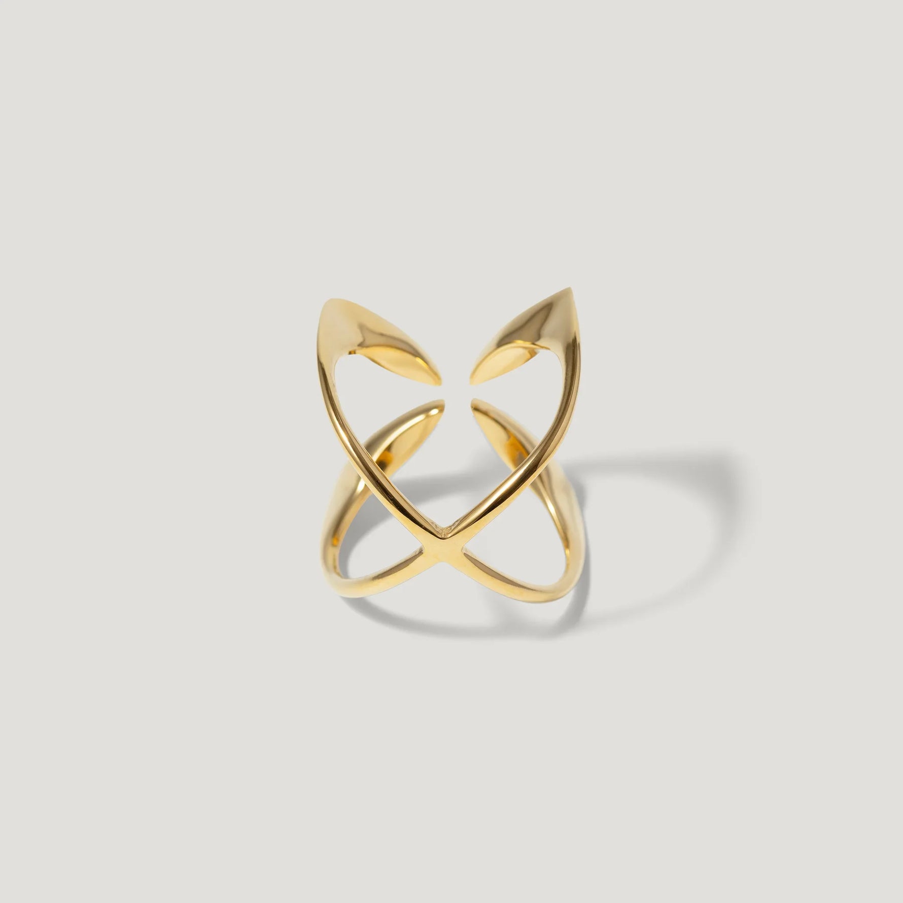 Modern open gold ring with sculptural, intersecting bands on a light background
