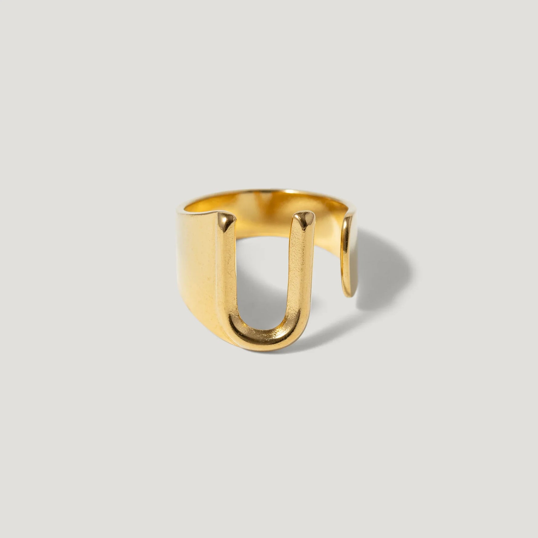 Minimalist open gold ring with a modern U-shaped design on a neutral background