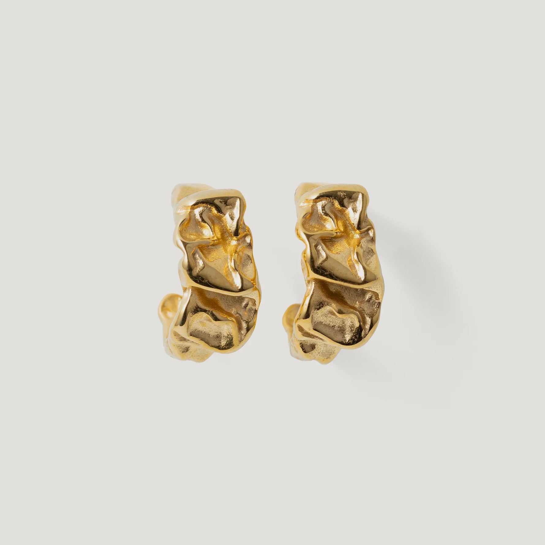 Pair of textured gold hoop earrings with organic, sculptural design on white background
