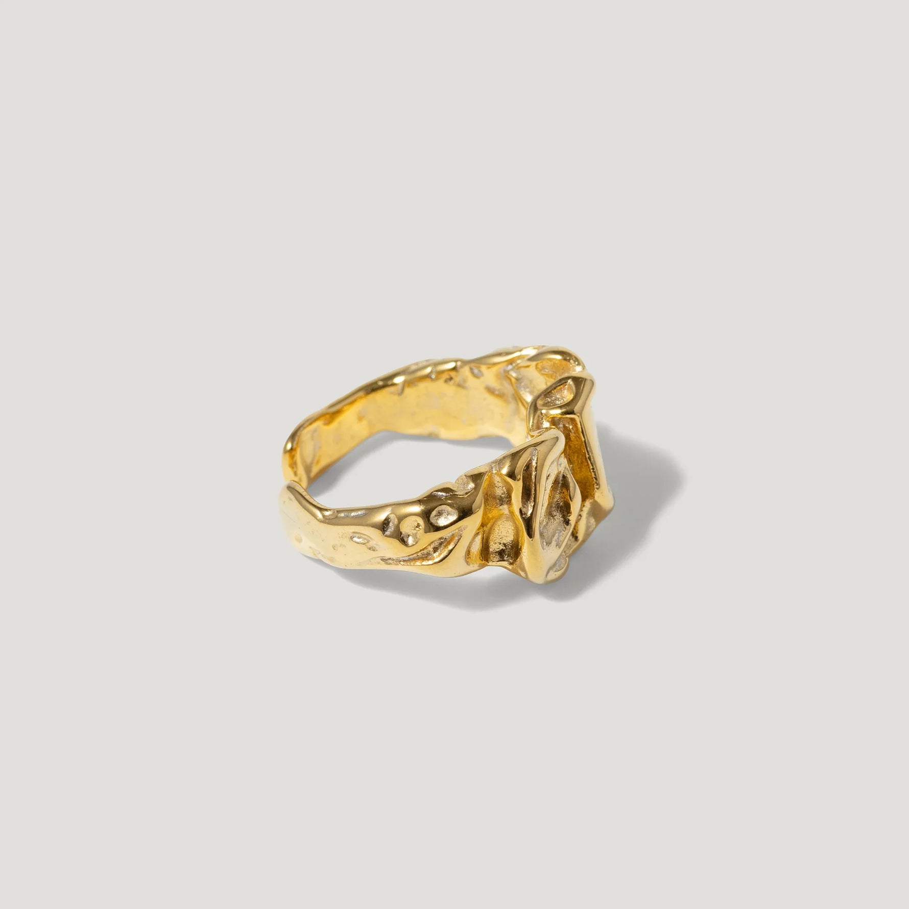 Textured gold ring with organic, sculptural design on light background