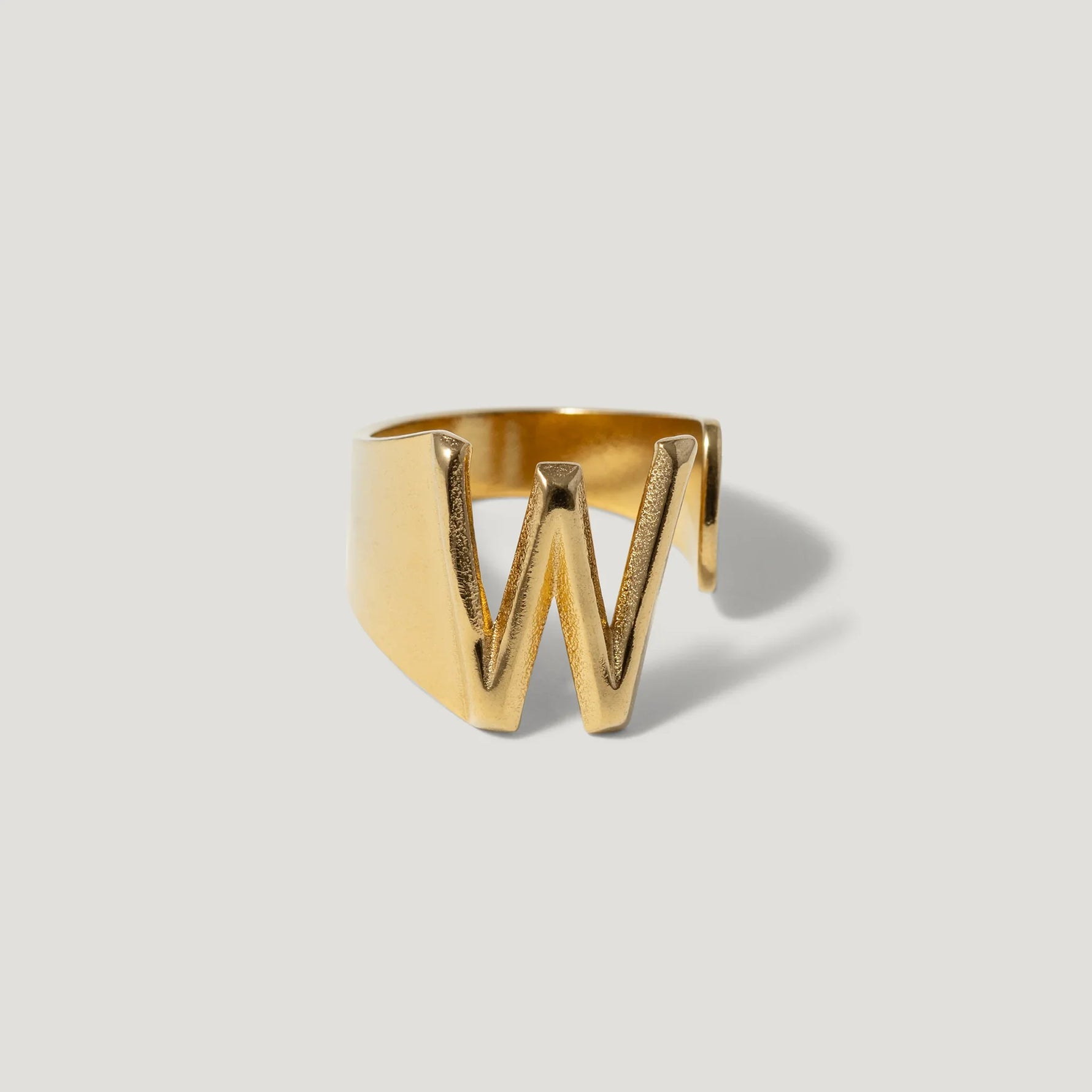 Gold ring with bold W initial design on a plain white background