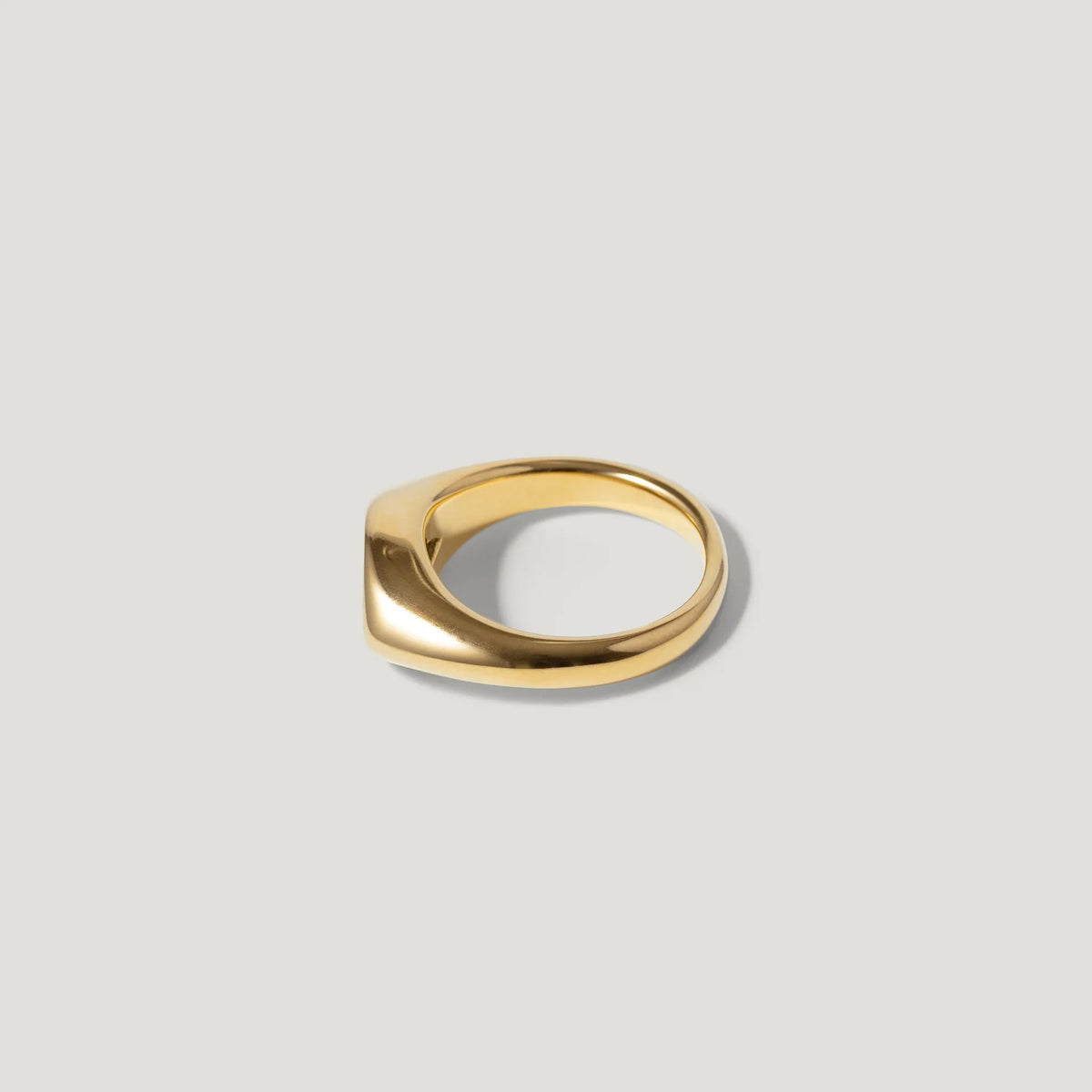 Minimalist gold signet ring with smooth, modern design on a light grey background