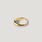 Minimalist gold signet ring with smooth, modern design on a light grey background