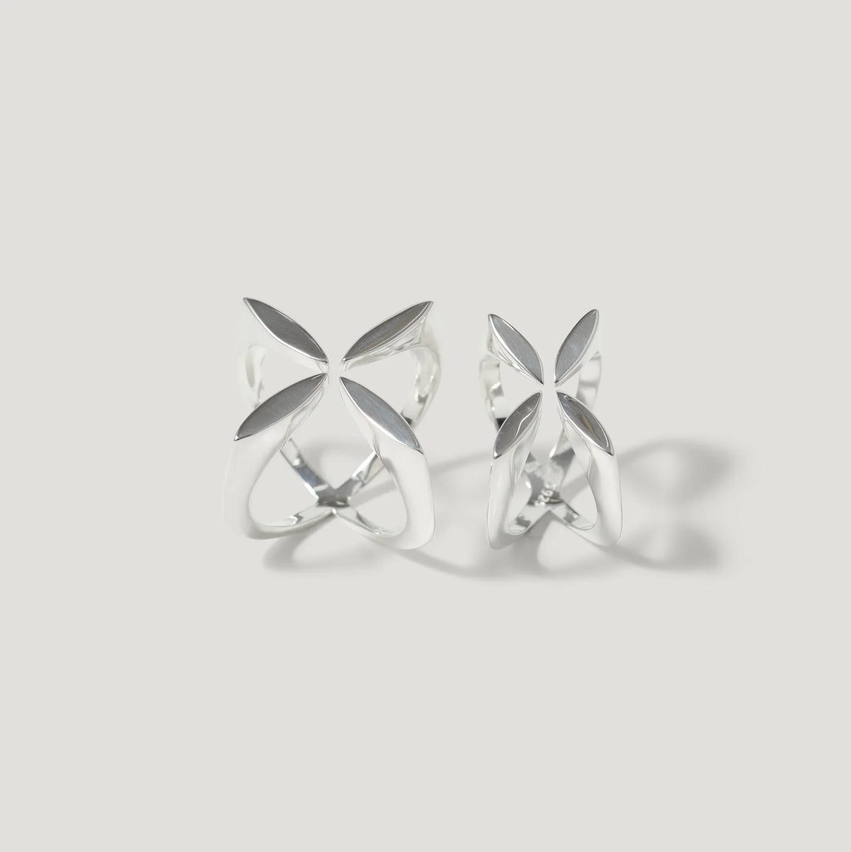 Pair of openwork silver rings with geometric petal design on light background