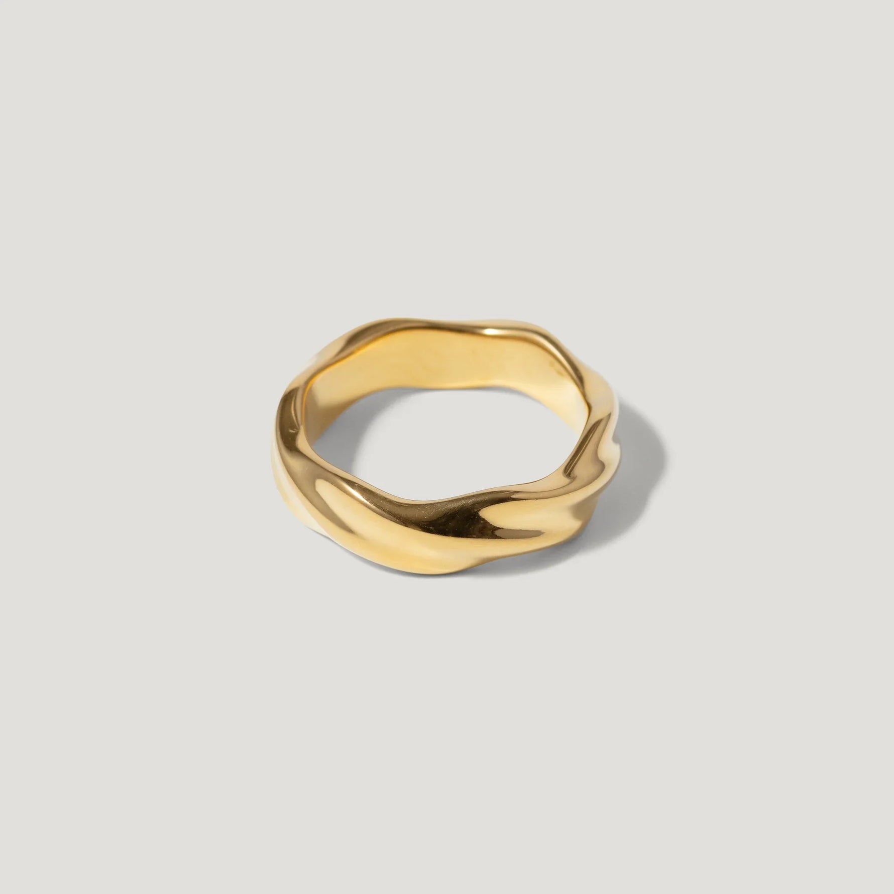 Polished gold wavy band ring with organic shape on a light background