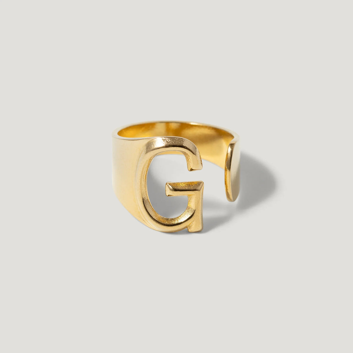 Gold open band ring with a bold letter G design on a light background