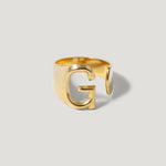 Gold open band ring with a bold letter G design on a light background