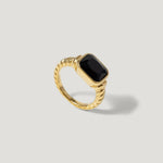 Gold ring with twisted band and rectangular black gemstone on light background
