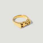 Gold ring with bold block letters spelling BRO on a neutral background