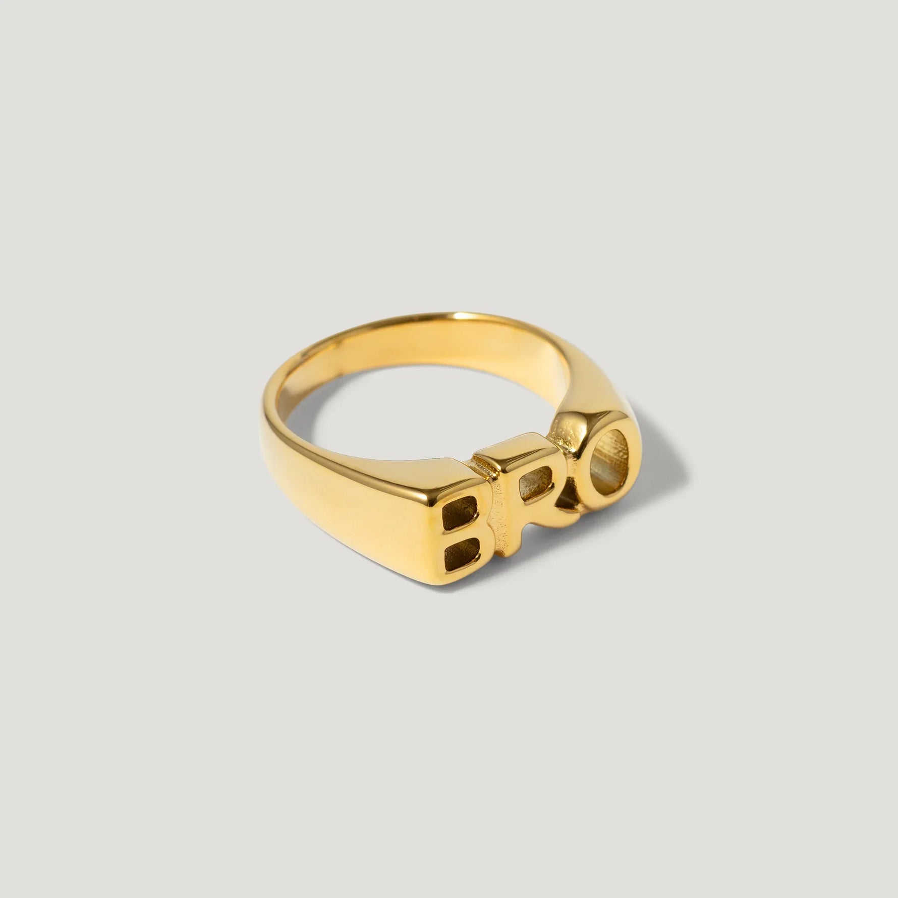 Gold ring with bold block letters spelling BRO on a neutral background