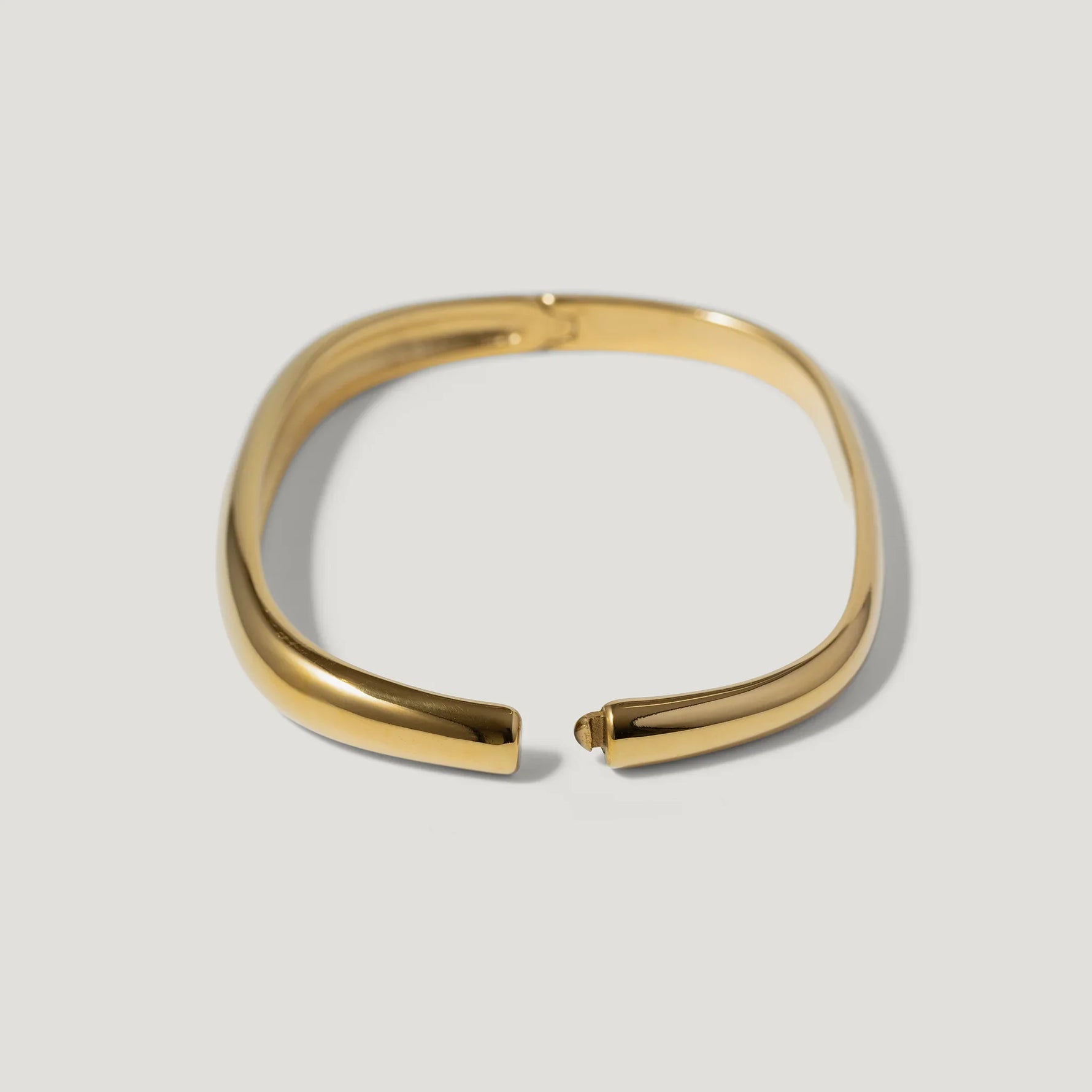 Elegant gold cuff bracelet with smooth, minimalist design on a light background
