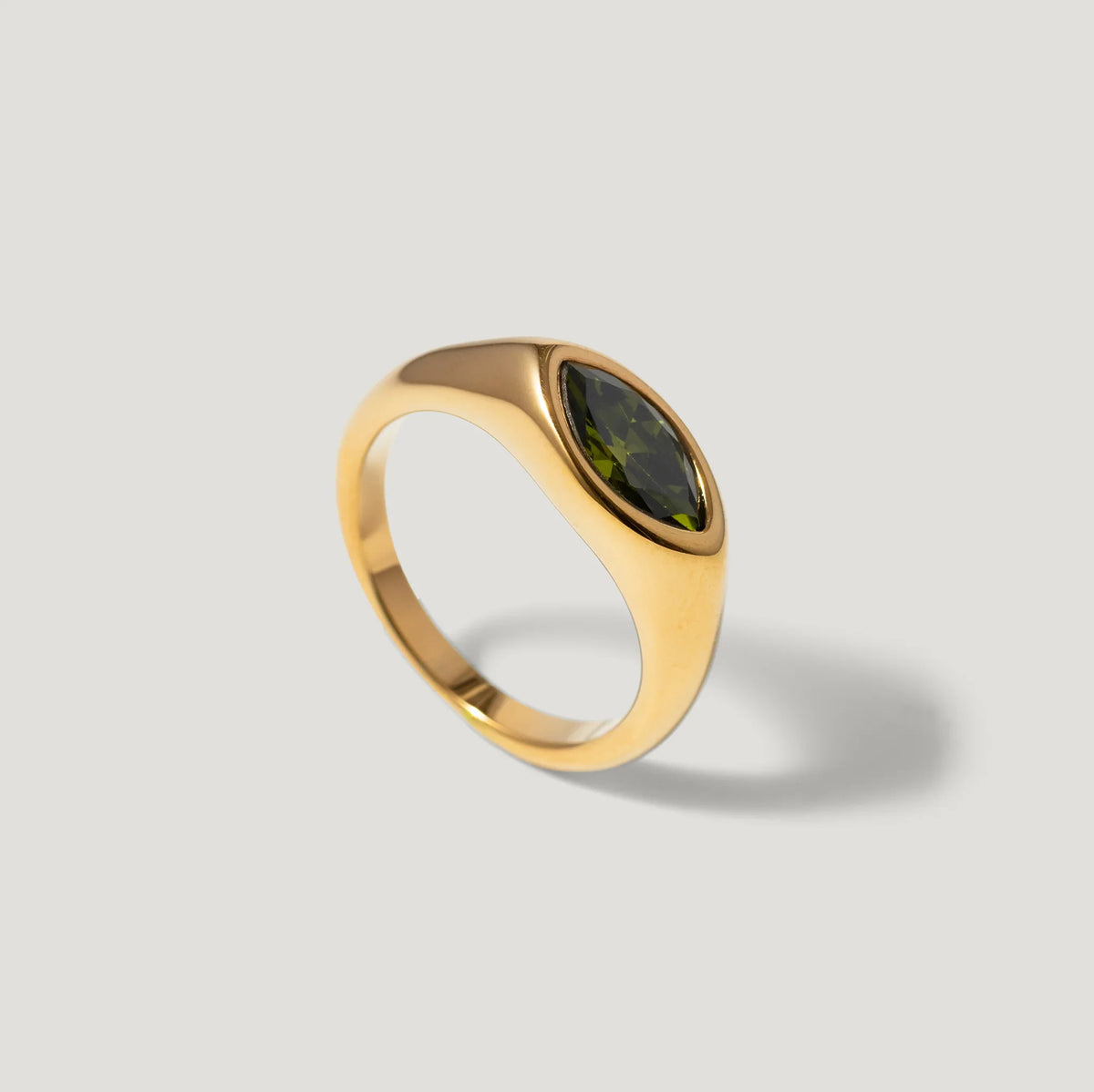 Gold ring with marquise-cut green gemstone on a light grey background
