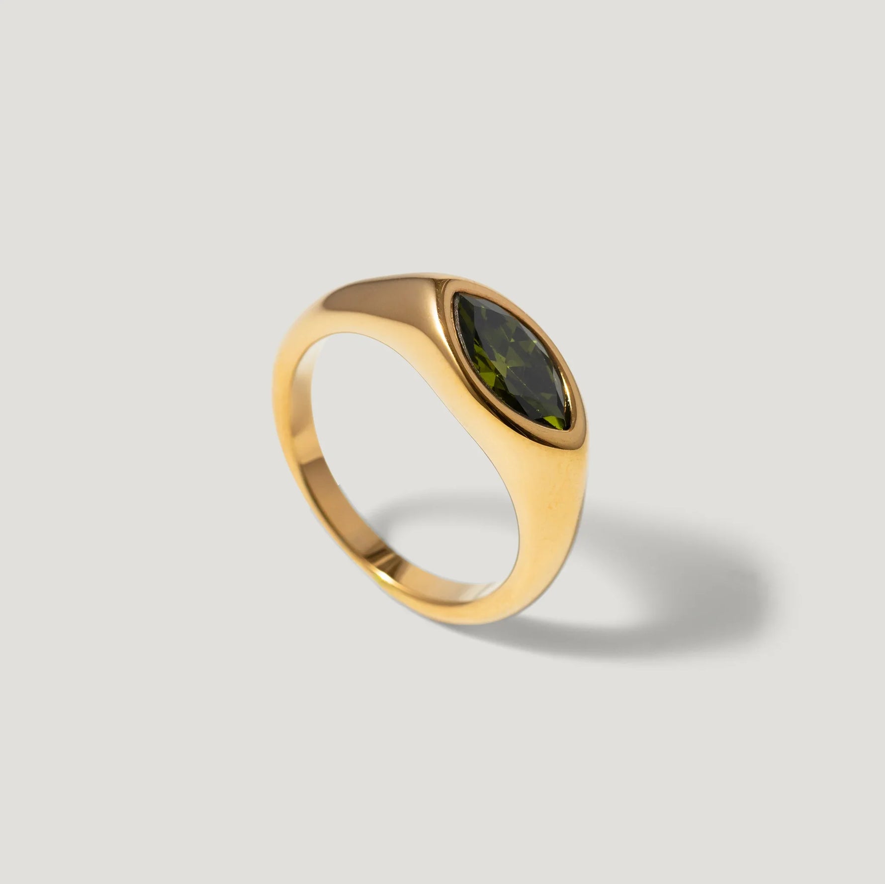 Gold ring with marquise-cut green gemstone on a light grey background