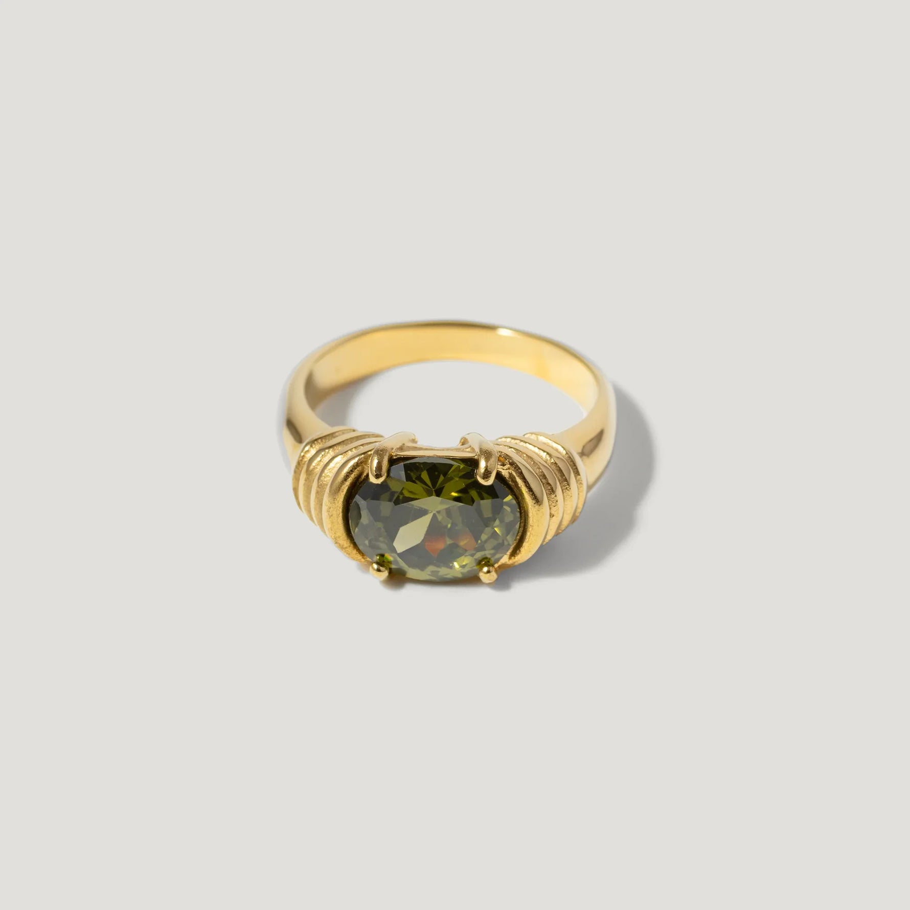 Gold ring with oval green gemstone and textured detailing on a light background