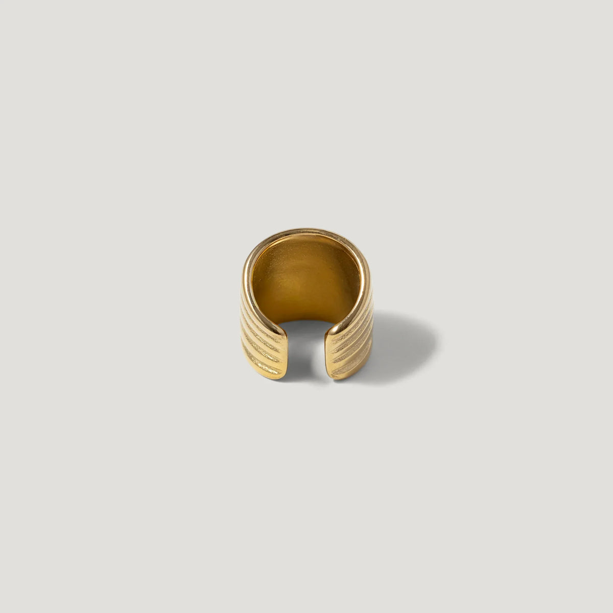 Gold open band ring with textured grooves on a neutral background