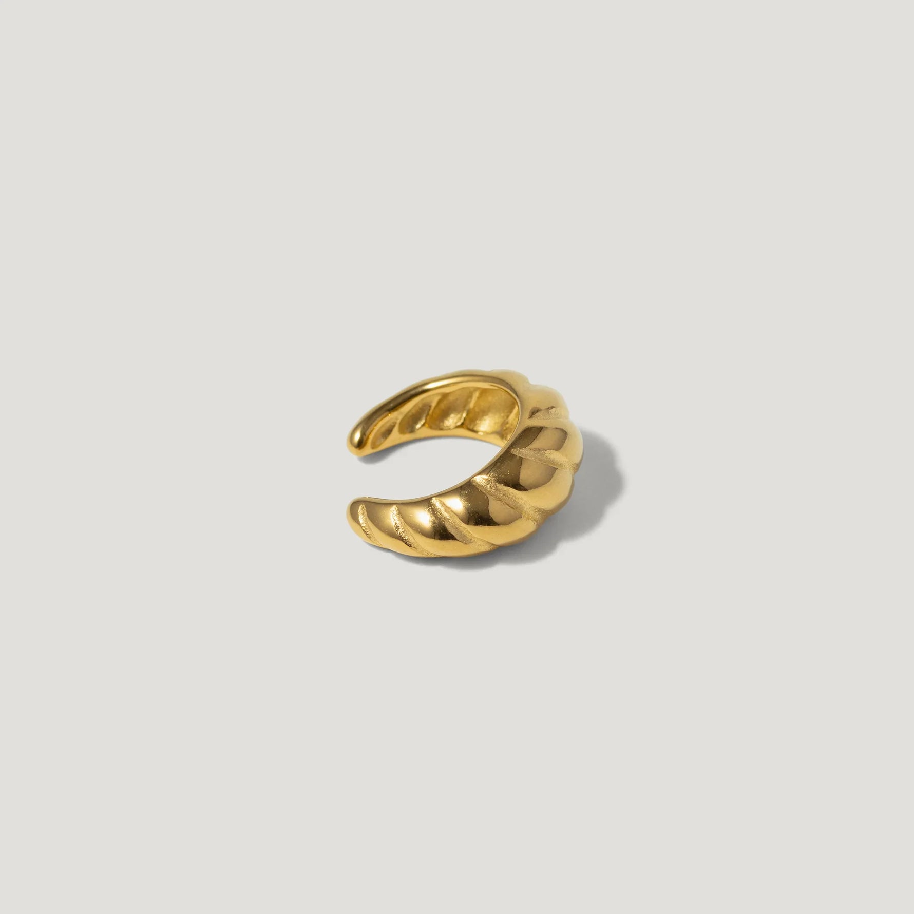 Twisted gold ear cuff with a sculpted, open design on a neutral background