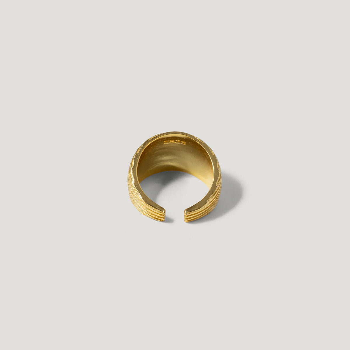 Textured gold open band ring with engraved details on a light background