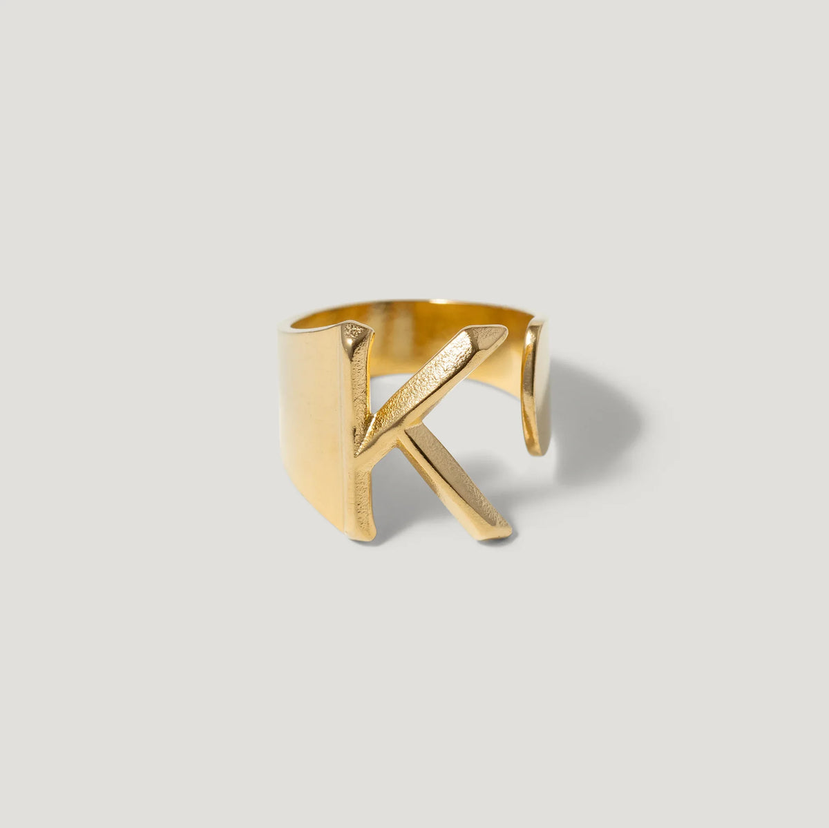 Gold open band ring with a bold letter K initial design on a light background