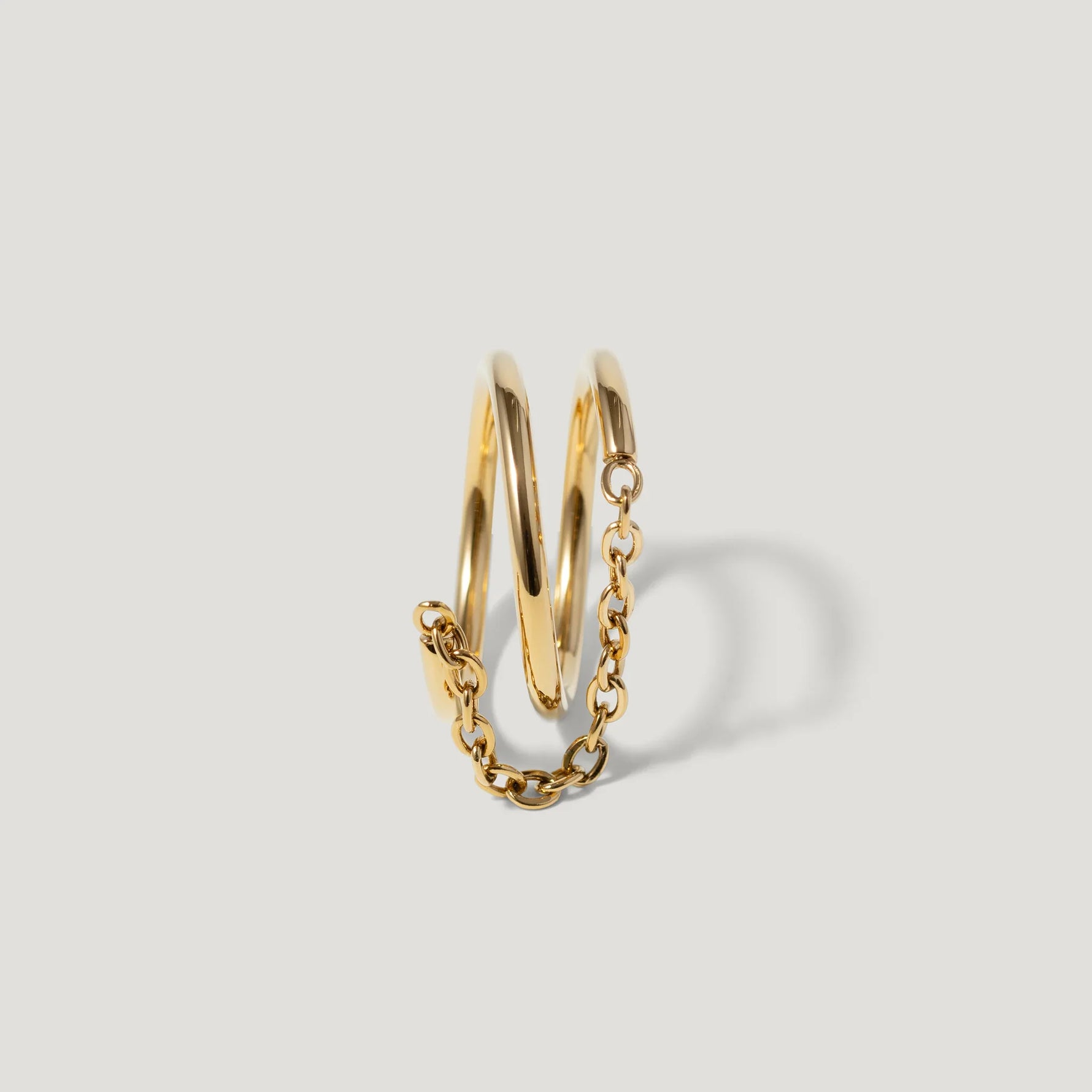 Gold spiral ring with attached chain on white background, modern jewelry design