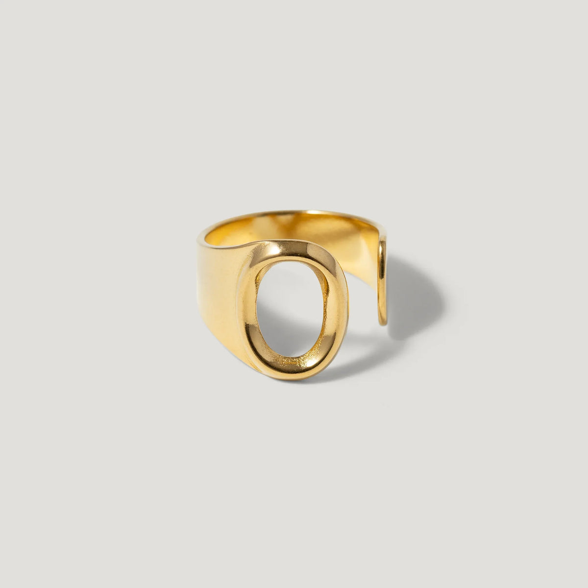 Minimalist open gold ring with oval cutout on light grey background