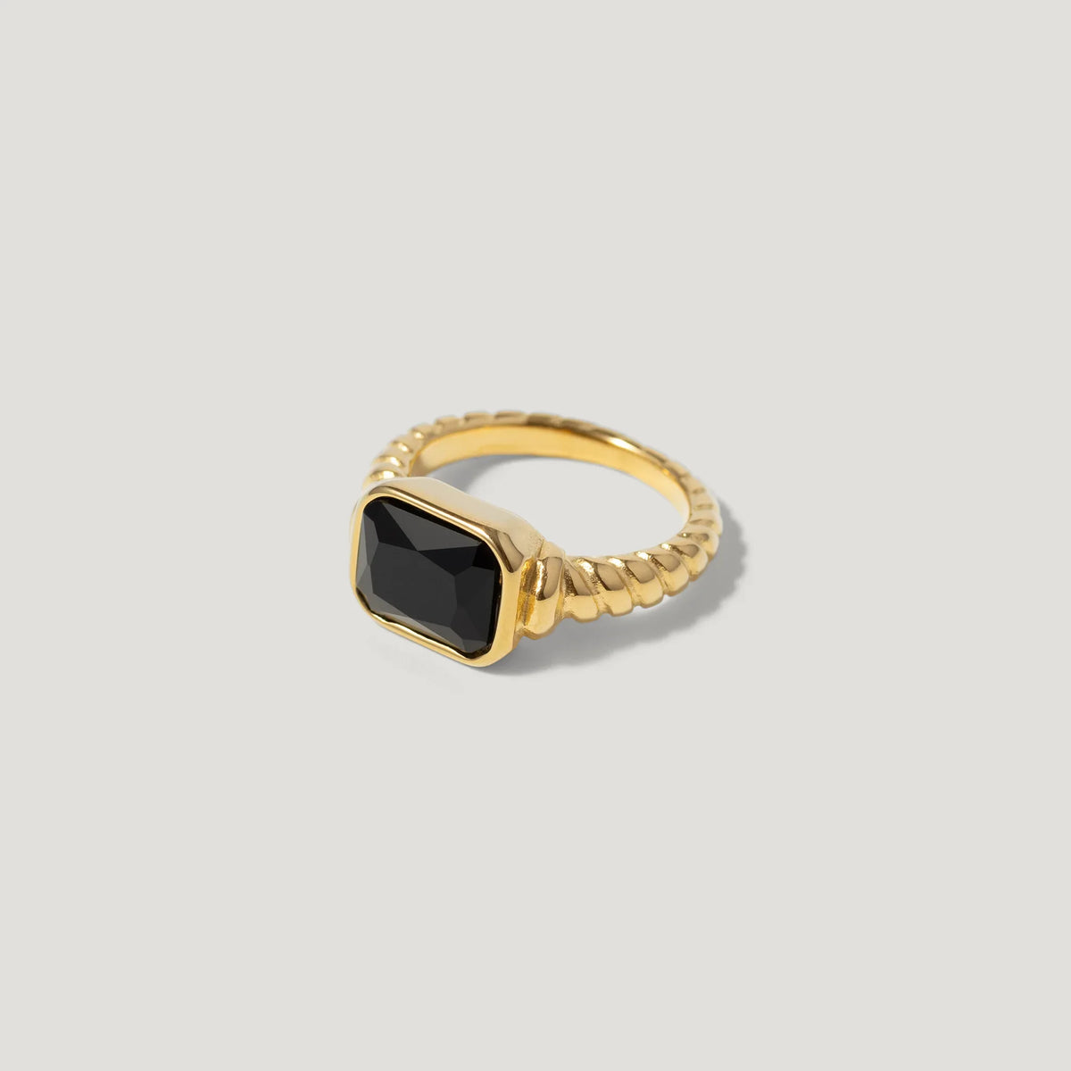 Gold ring with twisted band and rectangular black gemstone on light background