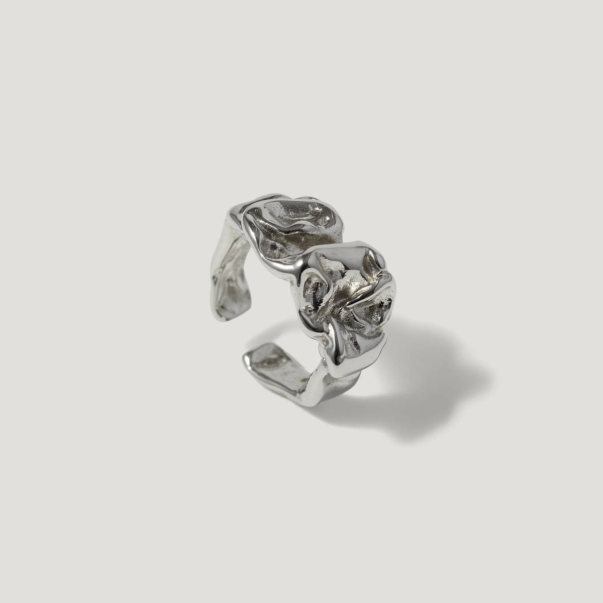 Silver sculpted open ring with organic, textured design on plain background