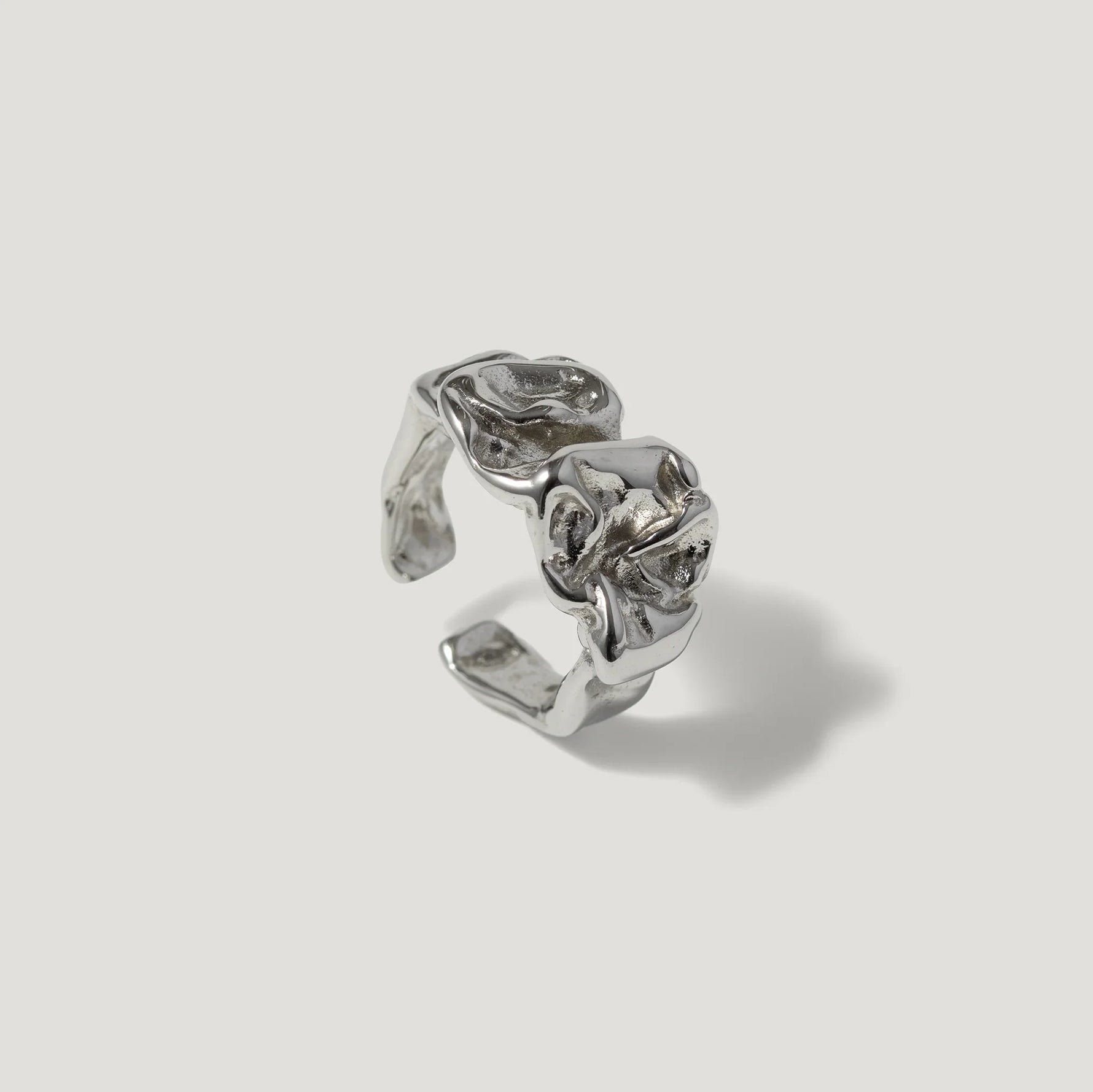 Silver sculpted open ring with organic, textured design on plain background