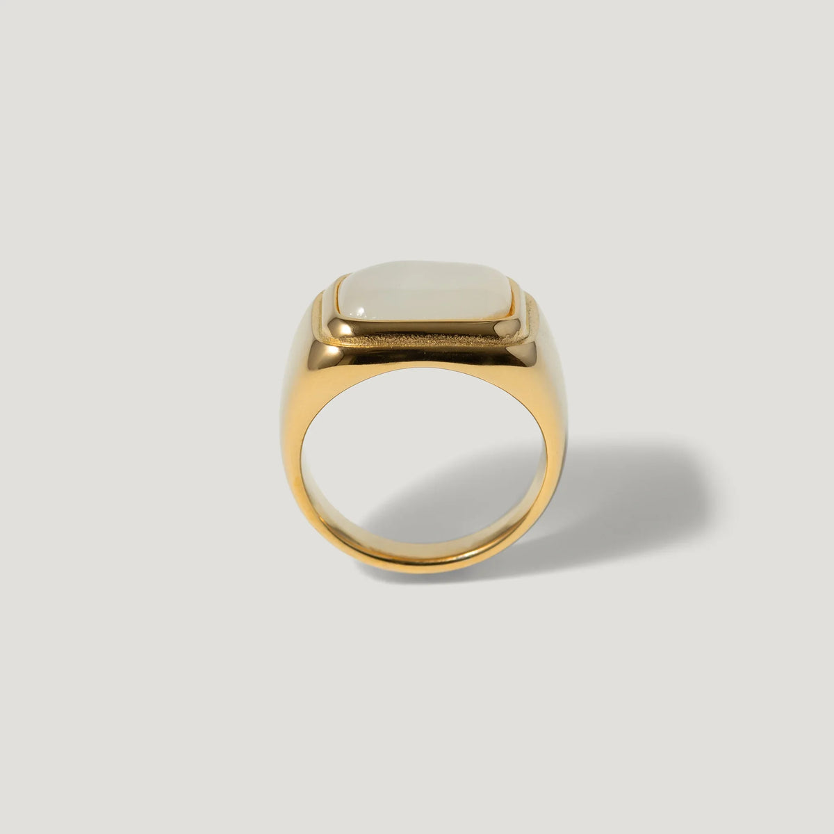 Gold signet ring with a square white stone on a plain light background