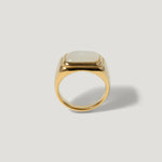 Gold signet ring with a square white stone on a plain light background