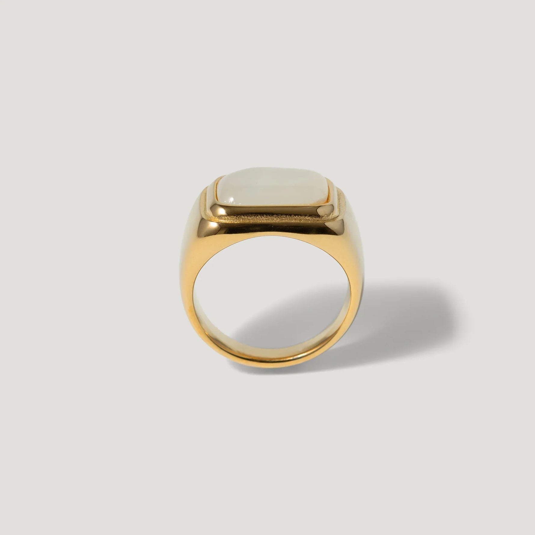 Gold signet ring with a square white stone on a plain light background