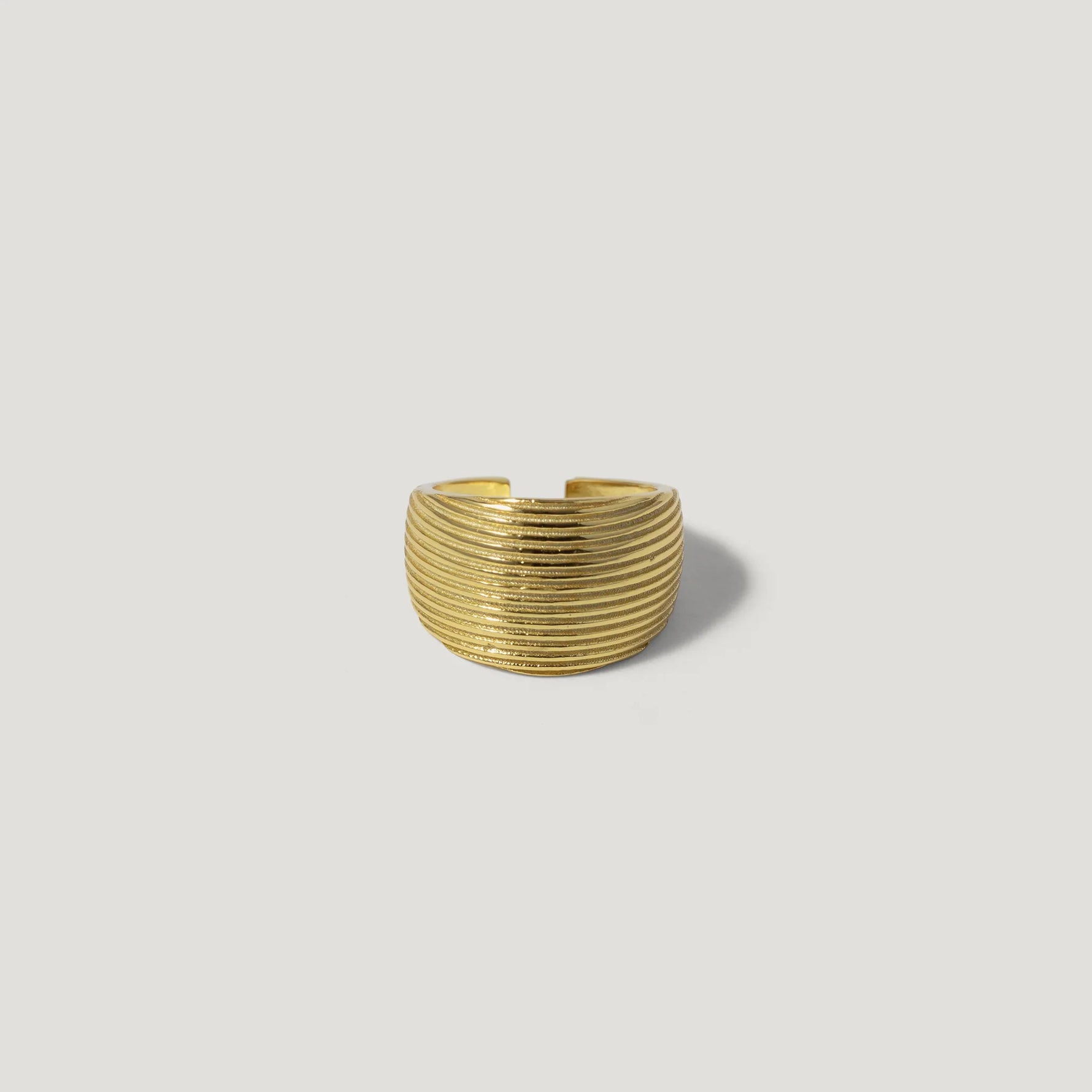 Textured gold wide band ring with grooved lines on a light neutral background