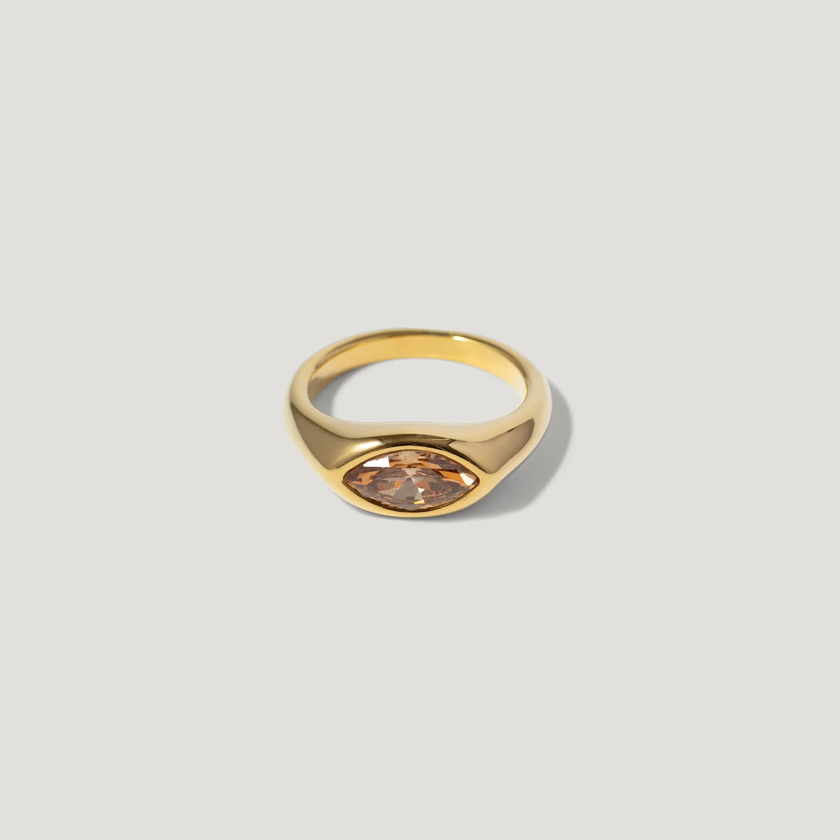 Gold ring with marquise-cut peach gemstone on neutral background