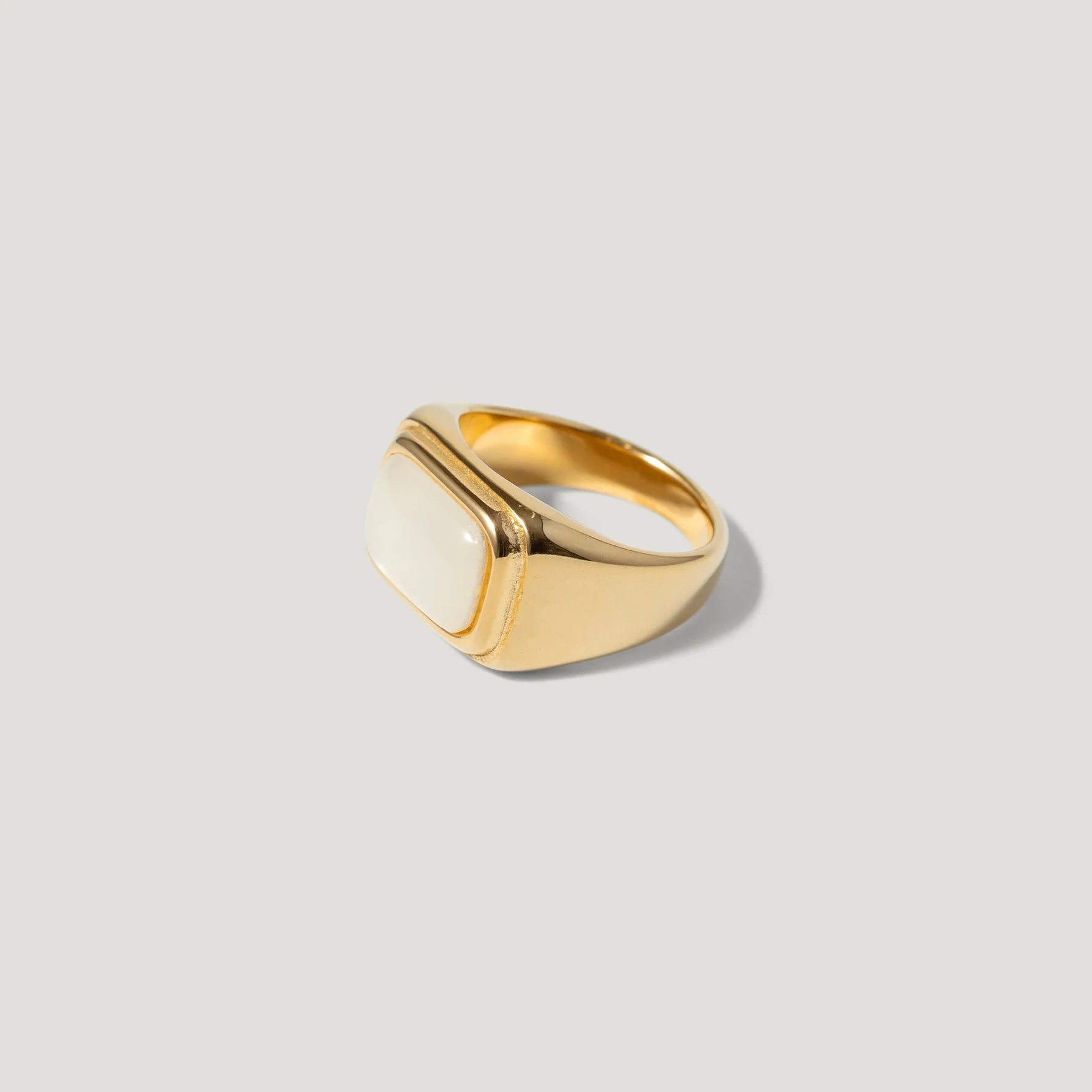 Gold signet ring with rectangular white stone on plain background