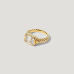 Gold twisted band ring with large square clear gemstone on neutral background
