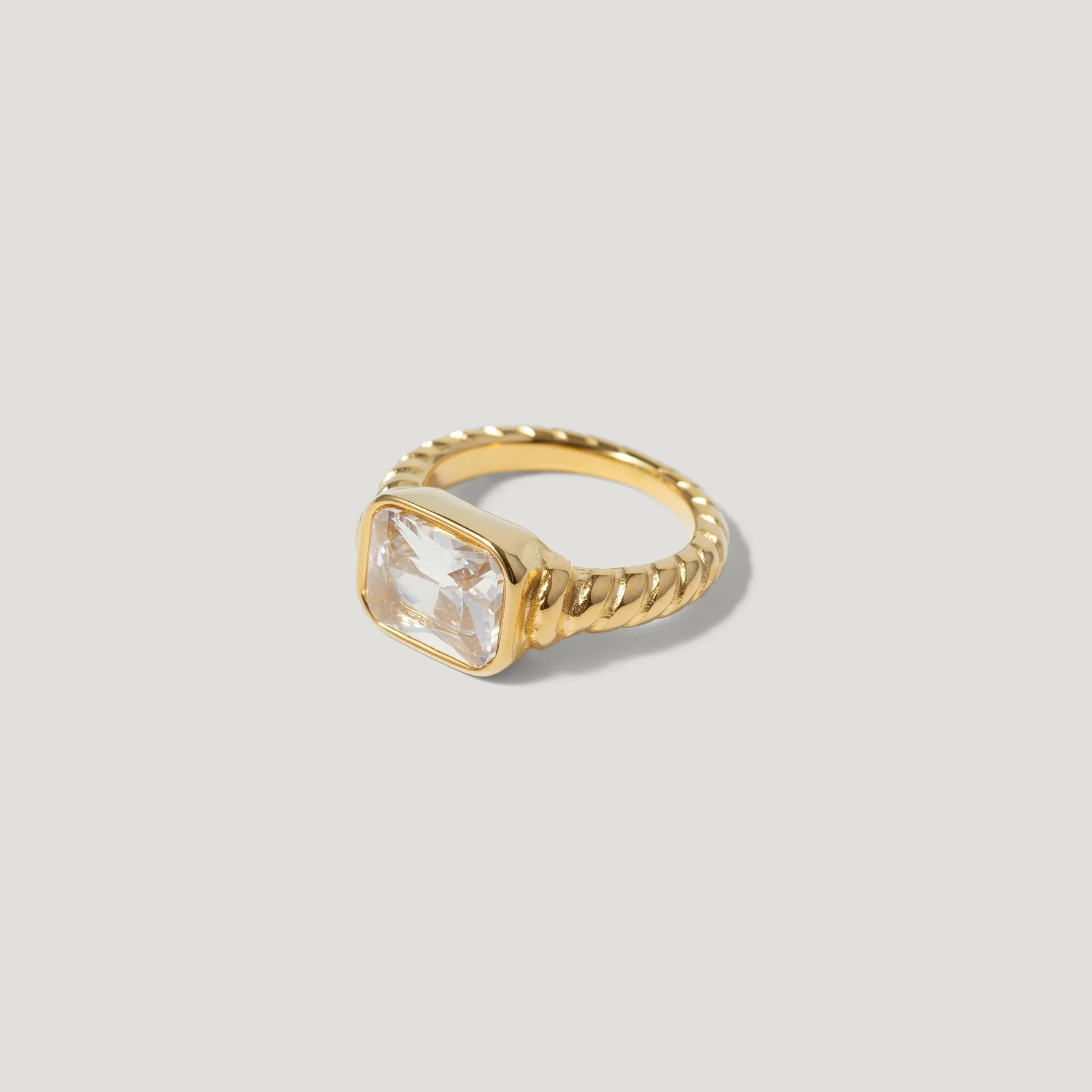 Gold twisted band ring with large square clear gemstone on neutral background