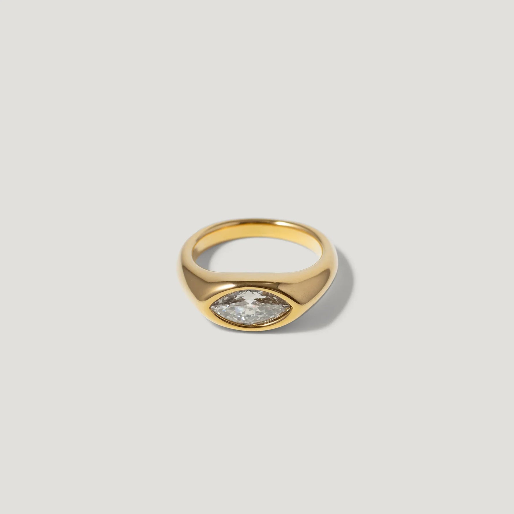 Gold signet ring with marquise-cut clear gemstone on a plain light background
