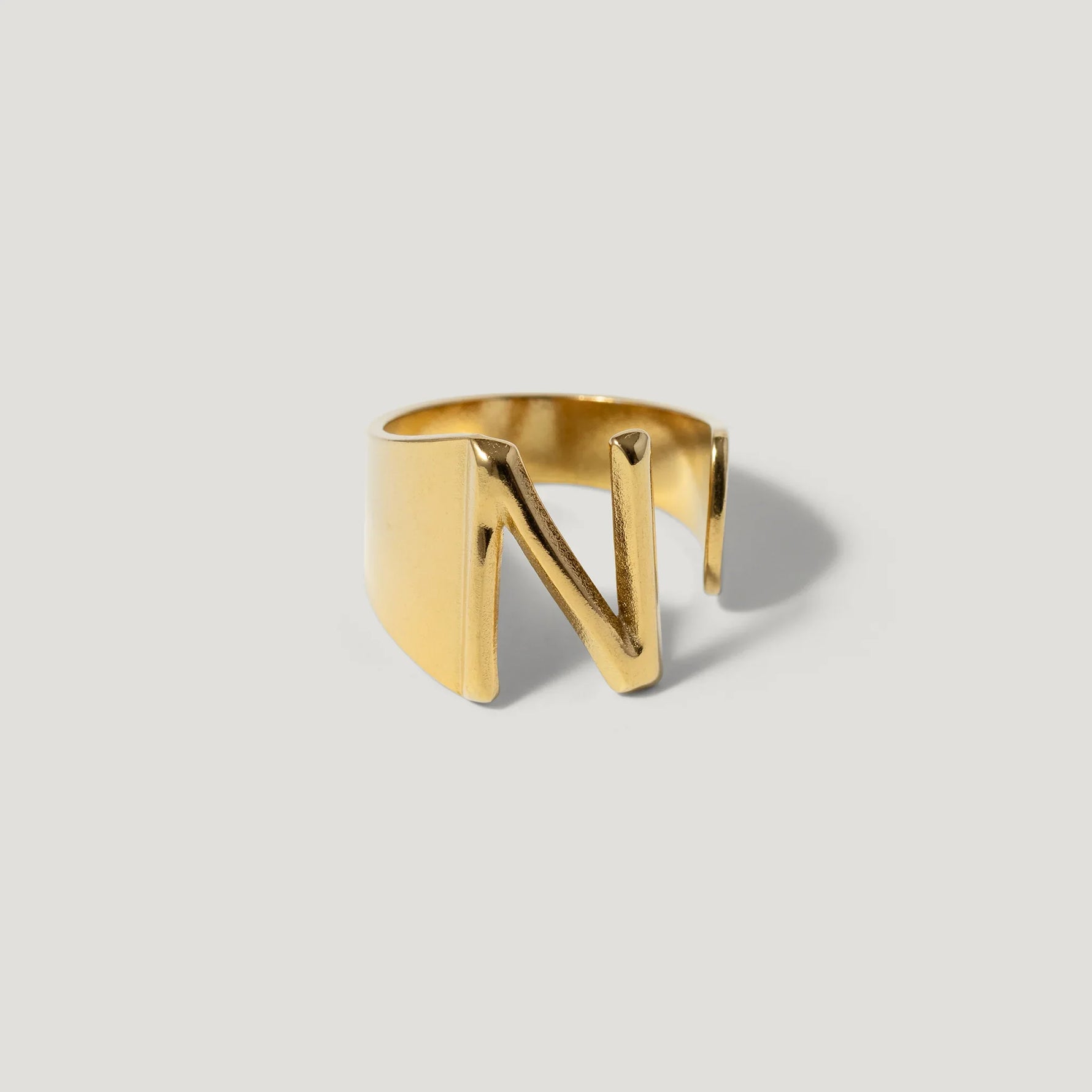 Gold ring with bold cut-out letter N, modern jewelry design on neutral background