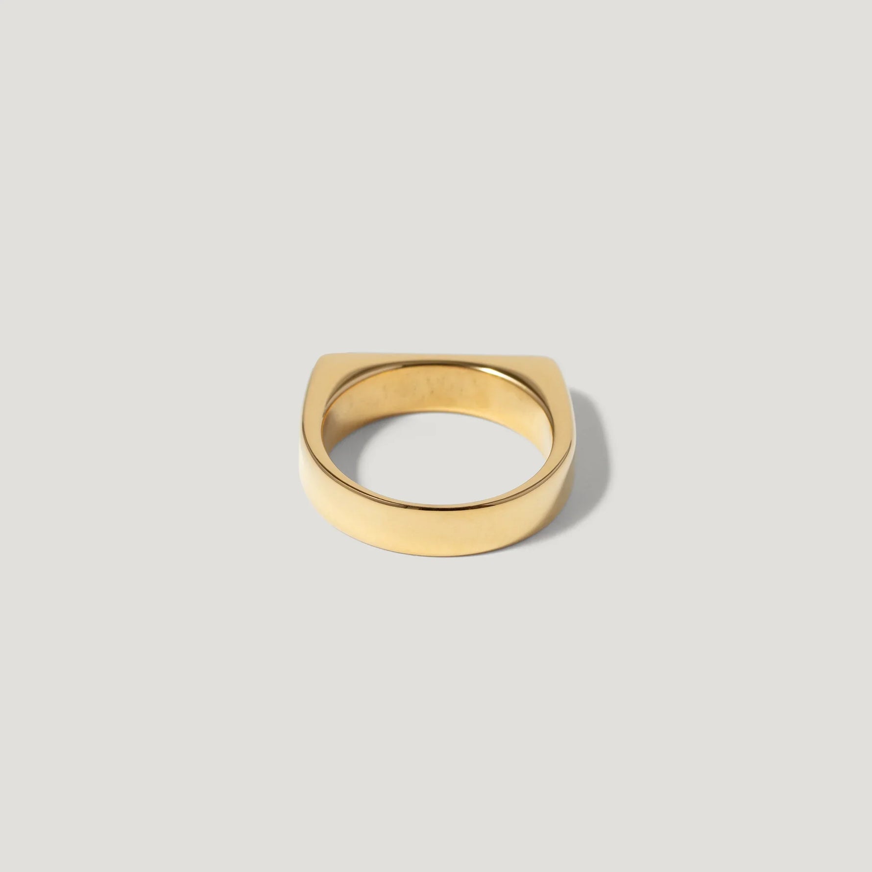 Minimalist gold ring with a flat square edge on a plain light background