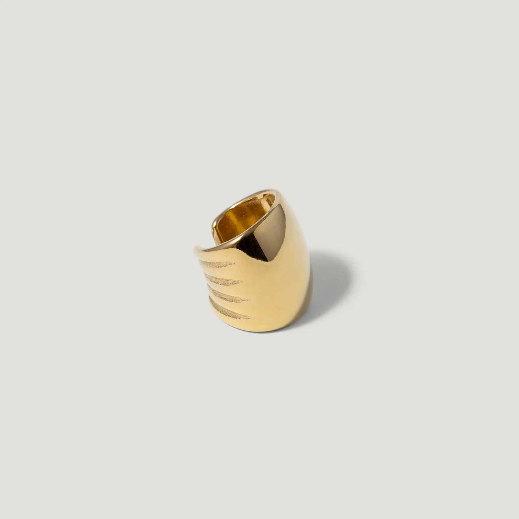 Wide gold statement ring with engraved lines on smooth surface, minimalist jewelry design